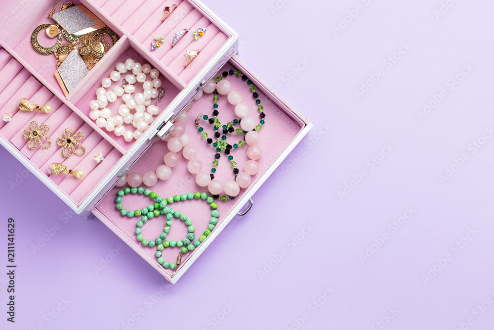Open jewelry box with neclaces, earrings and rings on pastel background. Top view Open jewelry box with neclaces, earrings and rings on pastel background. Top view