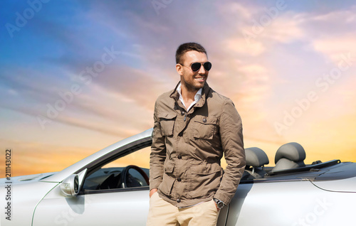 road trip, travel and people concept - happy man near convertible car over sky background © Syda Productions