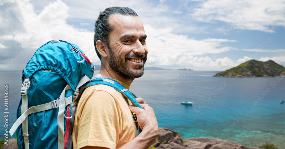 adventure, travel, tourism, hike and people concept - smiling man with backpack over background of seychelles island in indian ocean adventure, travel, tourism, hike and people concept - smiling man with backpack over background of seychelles island in indian ocean