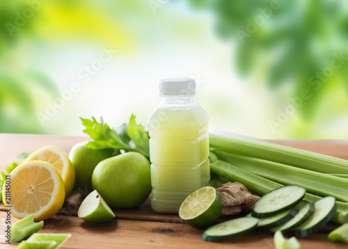 healthy eating, food, dieting and vegetarian concept - bottle with green juice, fruits and vegetables on wooden table over green natural background