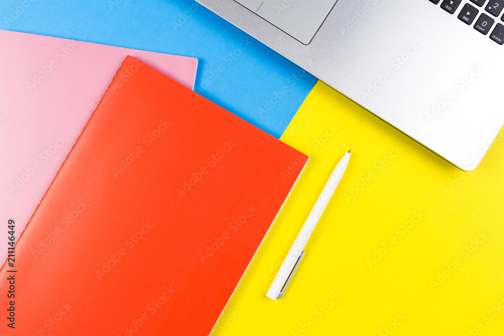 Top view of laptop computer, paper notebooks and white pen on blue and yellow color background Top view of laptop computer, paper notebooks and white pen on blue and yellow color background