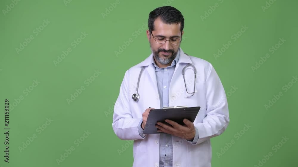 Handsome Persian bearded man doctor consulting while writing on clipboard Handsome Persian bearded man doctor consulting while writing on clipboard