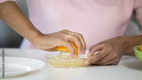 Woman juicing out orange with handheld juicer, taking care of health, nutrition