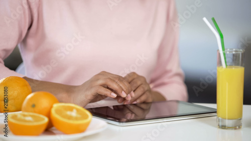 Woman using tablet at table with oranges, searching for nutritious diet, vitamin