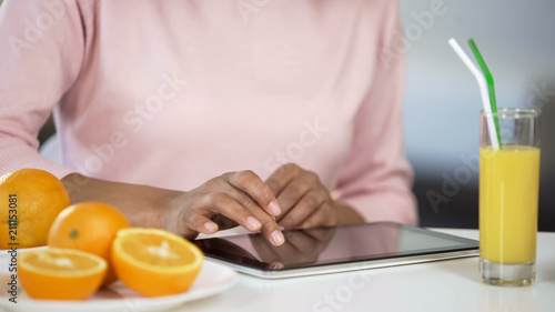 Girl typing on tablet, oranges and fresh juice on table, blogging about dieting