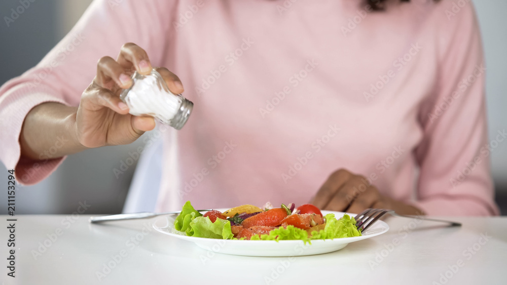 Woman adding too much salt to her food, unhealthy eating, dehydration problems