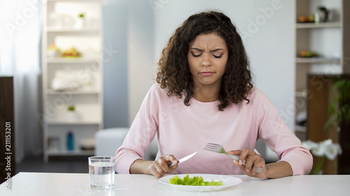 Принти на полотні Young woman forcing herself to eat salad, dissatisfaction, weight control diet