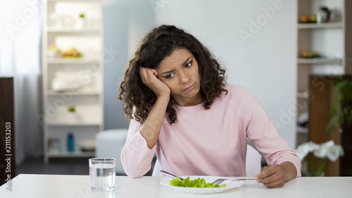 Foto Sad lady in front of green salad plate and glass of water on table, weight loss
