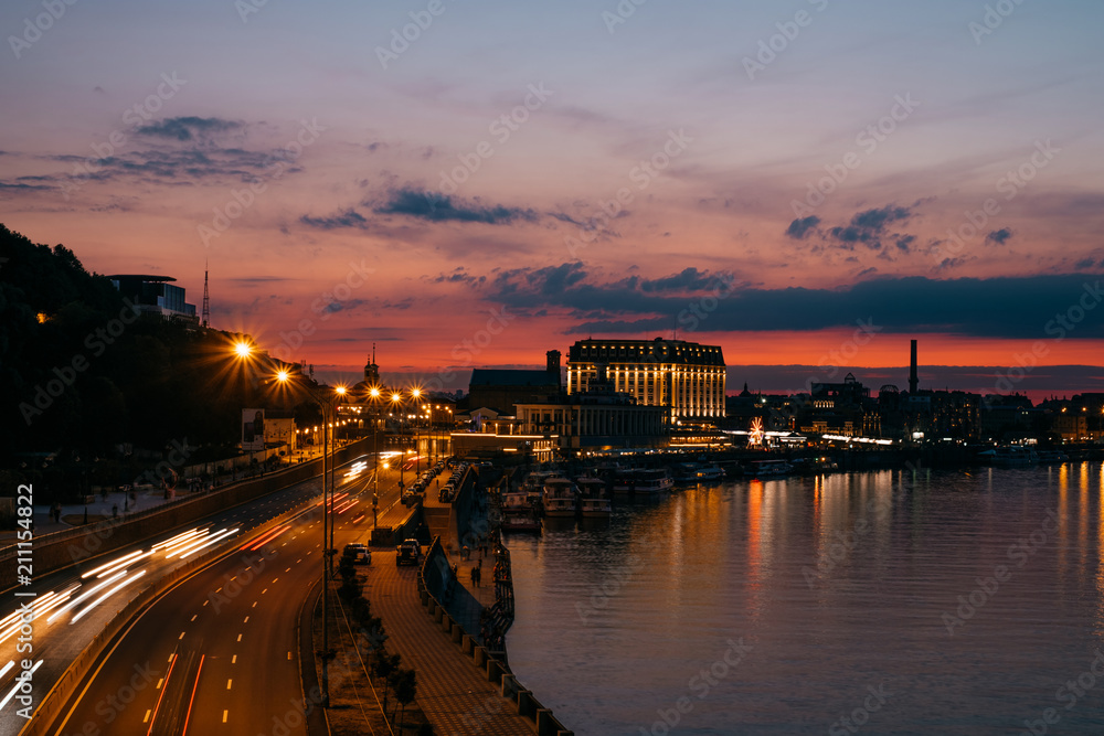 Kiev Kyiv city, the capital of Ukraine at night with beautiful sunset clouds, colorful illumination and reflection in Dnieper Dnipro river. Long exposure traffic light.