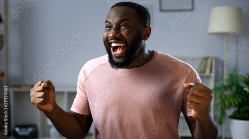 Foto Happy afro-american football fan watching match on tv at home, rejoicing goal