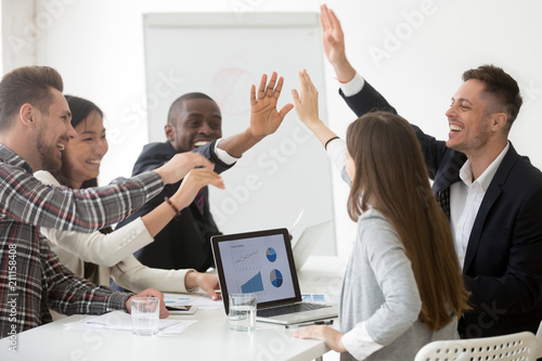 Excited diverse work team giving high five at board meeting, celebrating shared goal achievement, congratulating with win or good result, showing team spirit, unity. Concept of cooperation, rewarding photo