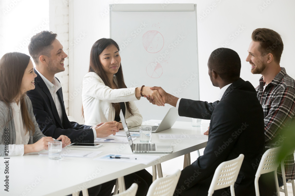 Smiling Asian female worker shaking hand of African American colleague at office business meeting, partners handshaking thanking for successful work negotiations. Concept of cooperation, partnership Smiling Asian female worker shaking hand of African American colleague at office business meeting, partners handshaking thanking for successful work negotiations. Concept of cooperation, partnership