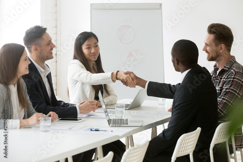 Smiling Asian female worker shaking hand of African American colleague at office business meeting, partners handshaking thanking for successful work negotiations. Concept of cooperation, partnership