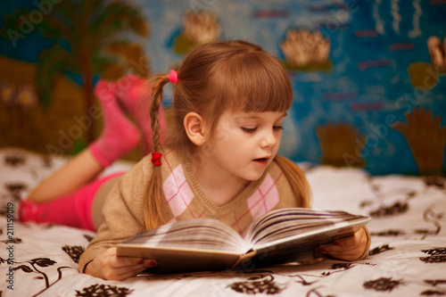 Little cheerful girl read book in bed. Concept of kids knowledge