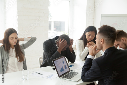 Disappointed diverse millennial team feeling despair because of bad results or falling statistics, upset colleagues shocked by negative bankruptcy news at company meeting, trying to solve problems. photo