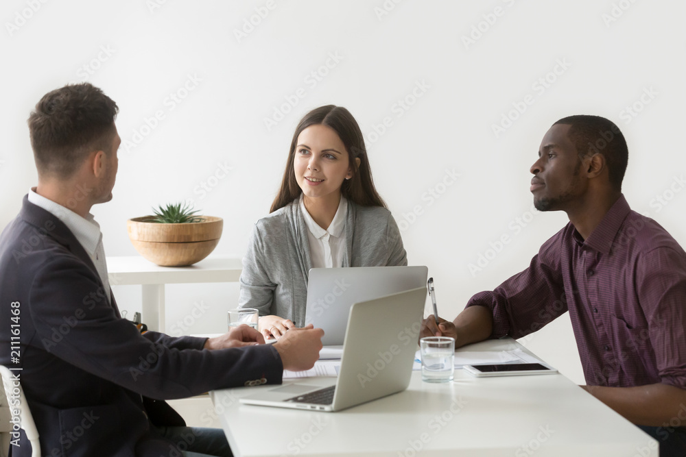 Obraz premium Three Millennial colleagues collaborating working together in coworking space with laptops and tablet, workers discussing business project, preparing reports on computers. Cooperation concept