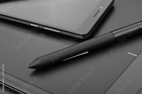 Smartphone and digital drawing tablet (also known as a digital art board) with a special pen-like stylus on a wooden table. Details of workplace of an digital graphics art designer