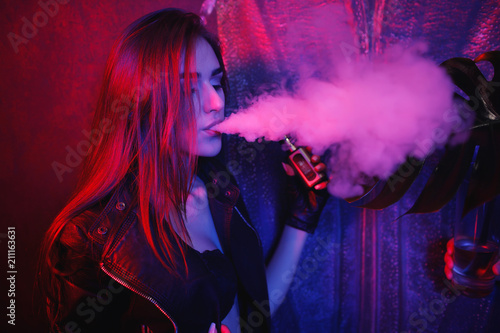 Trendy new vaping device, smoke e-liquid instead of nicotine cigarettes.  Tobacco free e-juice. Vaping concept. Woman with red lips. Girl inhaling  from an electronic cigarette. Modern girl smoking vape Stock Photo