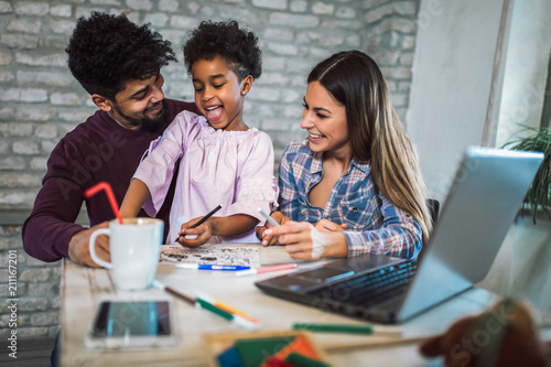 Mom and dad drawing with their daughter. Girl and mixed race parents having fun at home.