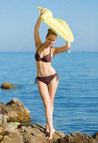 Young woman in brown bikini holds inflatable raft