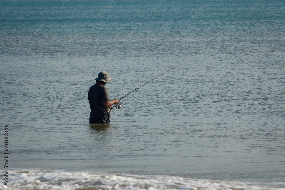 The fisherman catches fish in the sea on a fishing pole standing in water The fisherman catches fish in the sea on a fishing pole standing in water