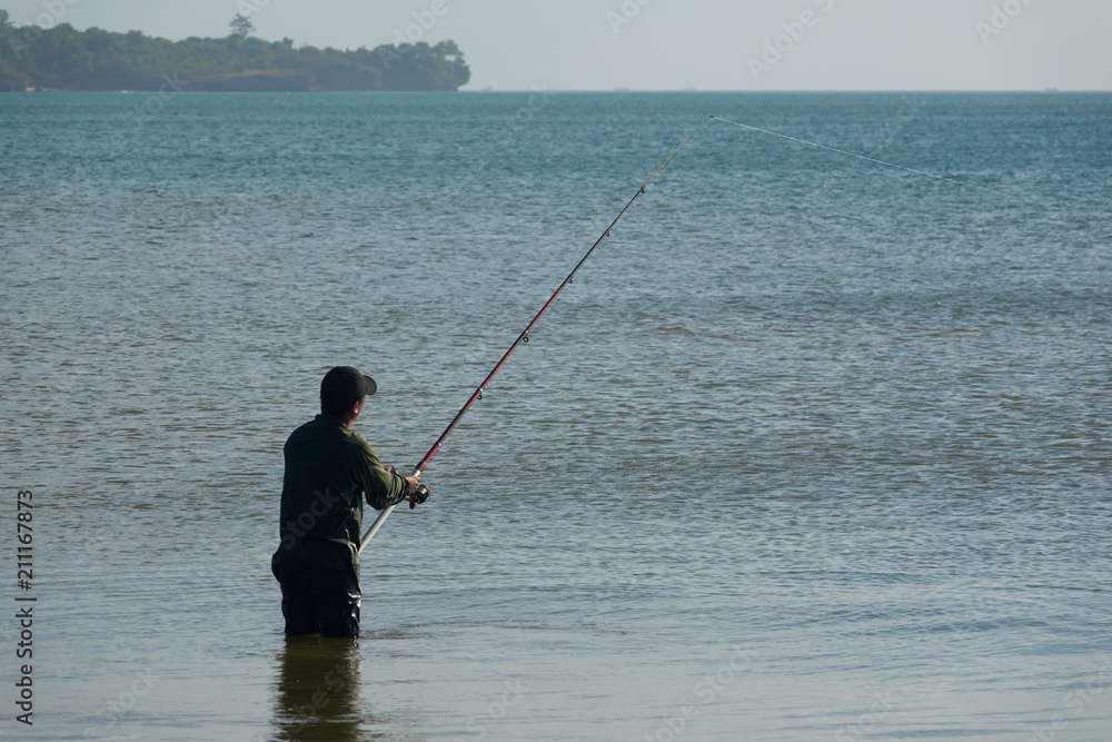 The fisherman catches fish in the sea on a fishing pole standing in water