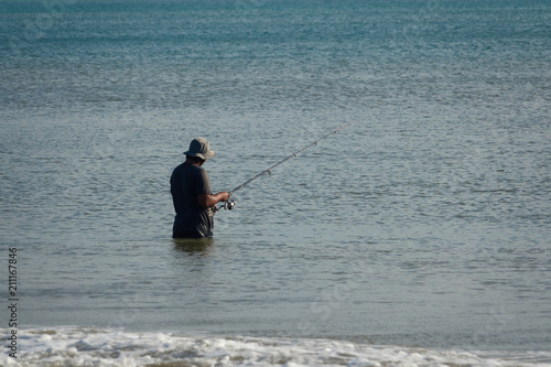 The fisherman catches fish in the sea on a fishing pole standing in water