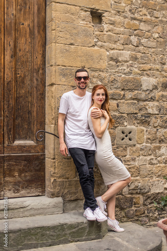 young beautiful couple, a girl with red hair and a white dress and a man in a white T-shirt are standing on an orange background in Italy