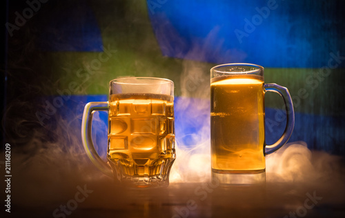 Creative concept. Beer glasses on table at dark toned foggy background with blurred view of flag of Sweden. Support your country with beer concept.