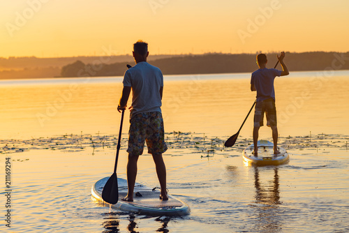 Men, friends sail on a SUP boards in a large river