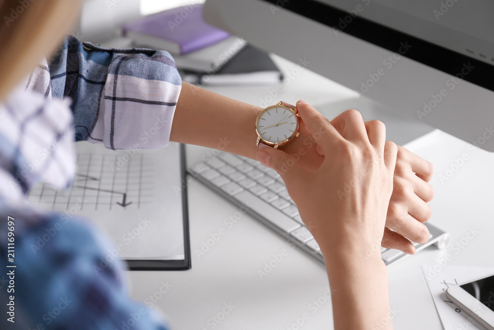 Young woman checking time on her wristwatch at workplace
