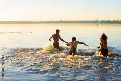 Joyful friends run into the water in a cloud of spray