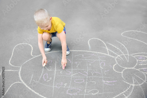 Little child drawing bunny with colorful chalk on asphalt