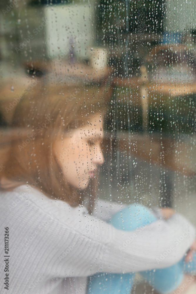 Depressed young woman near window, view from outside