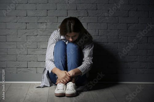 Lonely woman suffering from depression near brick wall