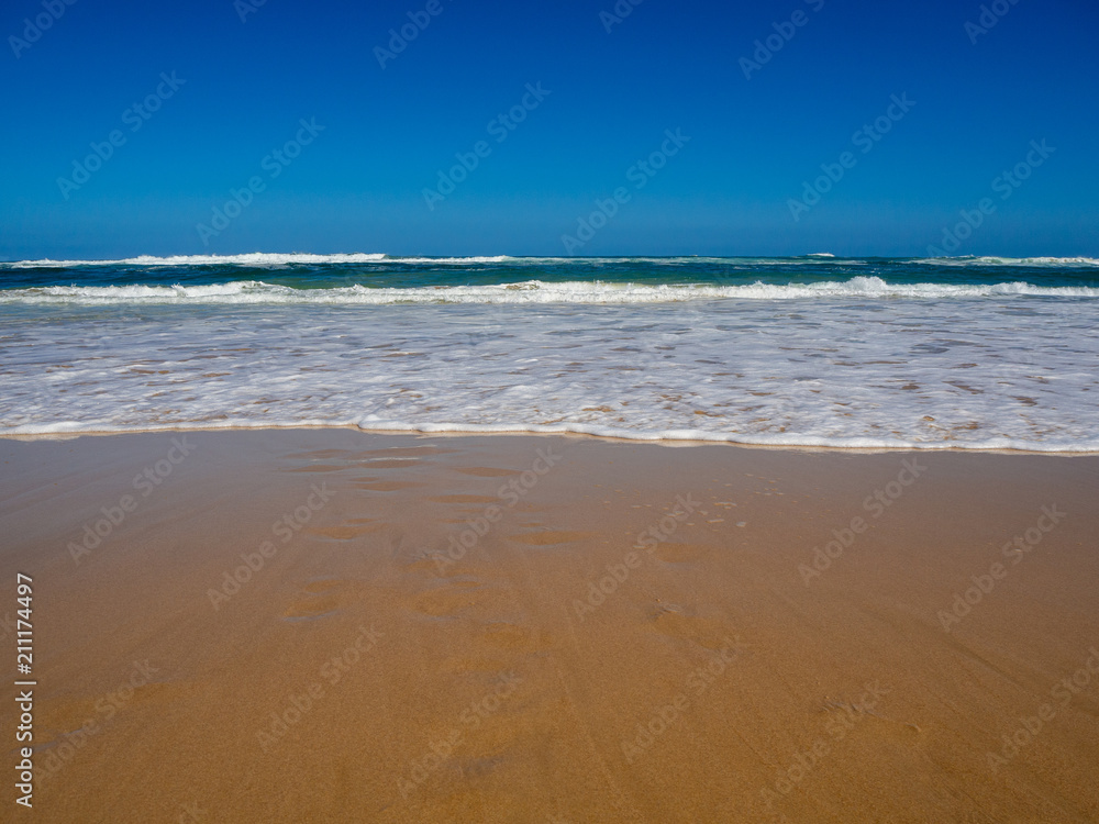 Beautiful empty paradise beach at the ocean with turquoise water, waves and yellow sand