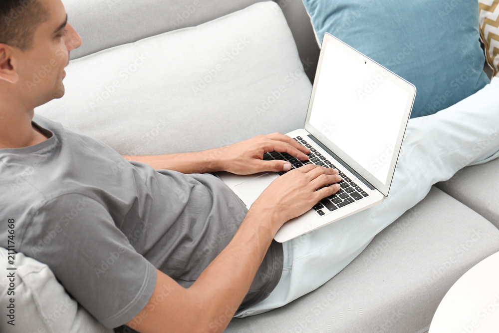 Naklejka premium Man in casual clothes using laptop on sofa at home