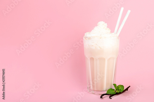 Glass with vanilla milk shake on color background