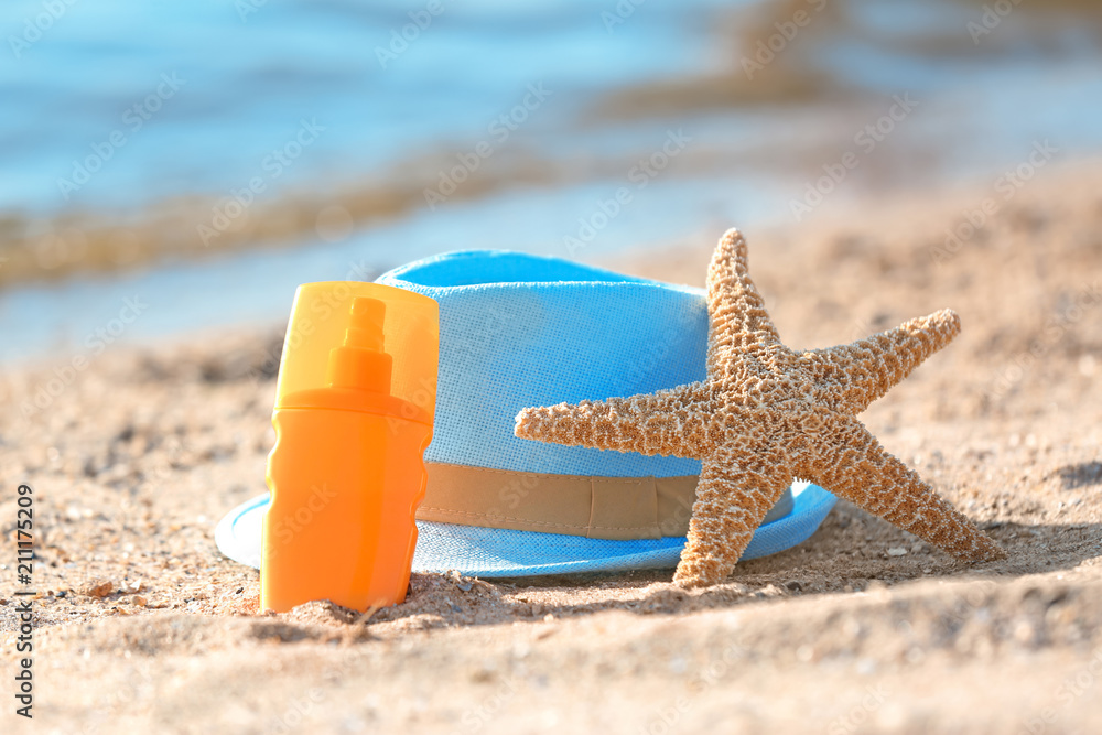 Starfish, bottle with sunscreen and hat on sand near sea. Beach object