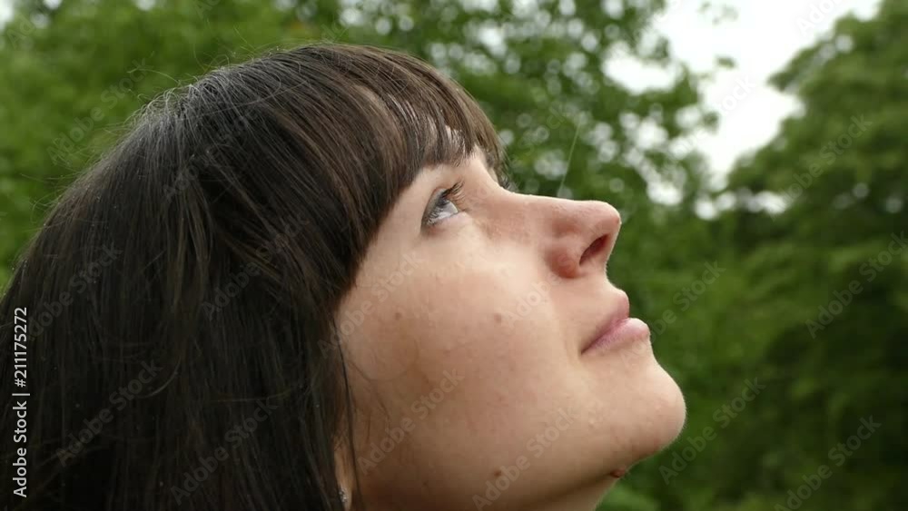 A beautiful girl is looking up at the falling drops of rain and clouds. Portrait of a girl on nature close-up. Minutes of happiness. Slow motion. A beautiful girl is looking up at the falling drops of rain and clouds. Portrait of a girl on nature close-up. Minutes of happiness. Slow motion.