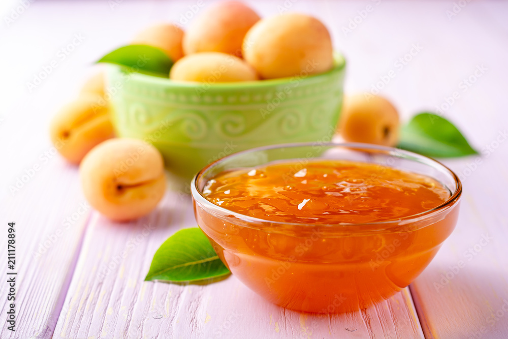 Apricot jam in glass bowl and fresh apricots on light purple wooden background Apricot jam in glass bowl and fresh apricots on light purple wooden background