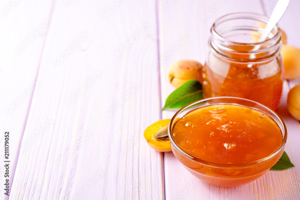 Apricot jam in glass bowl and fresh apricots on light purple wooden background Apricot jam in glass bowl and fresh apricots on light purple wooden background