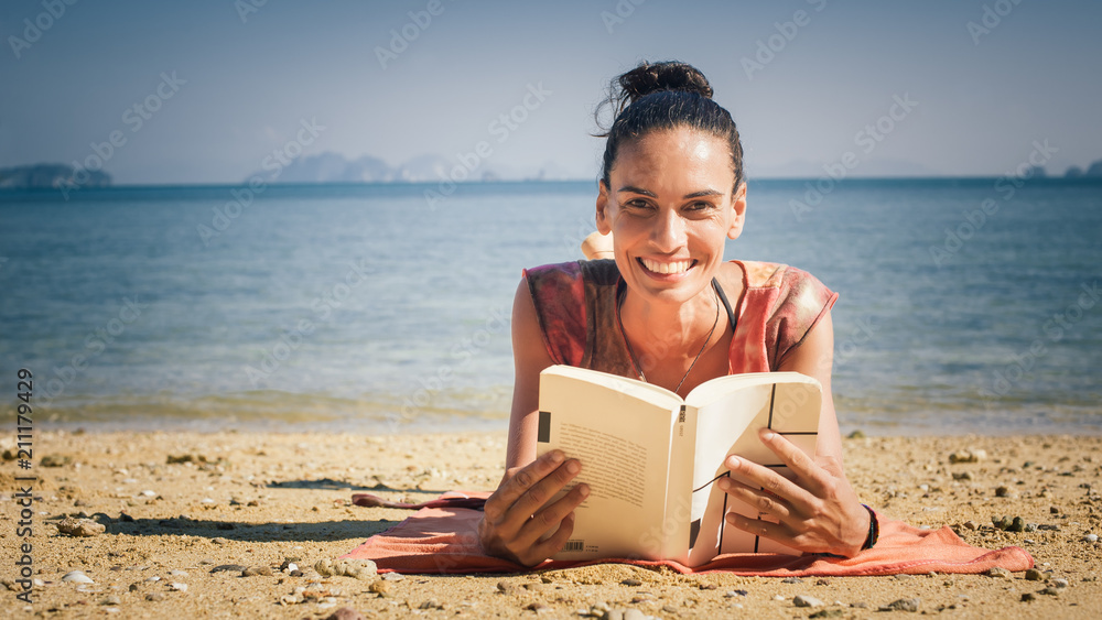 Woman reading book while enjoying the sunshine at the beach