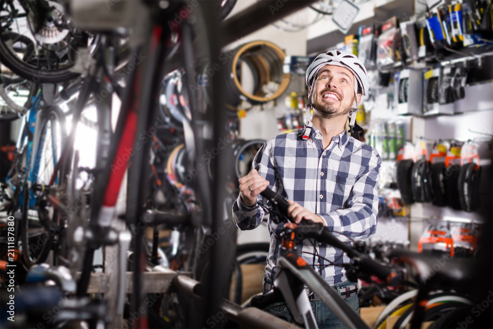 admiring man in helmet chooses for himself sports bike in bicycle shop