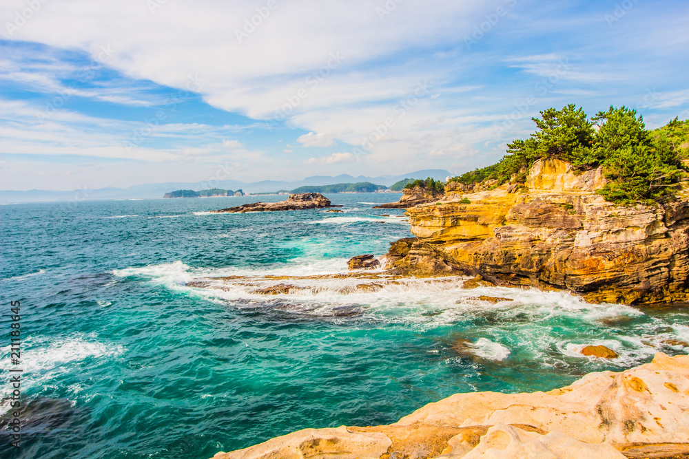 Landscape of the sea with rocks in the foreground and islands and blue sky in the background.