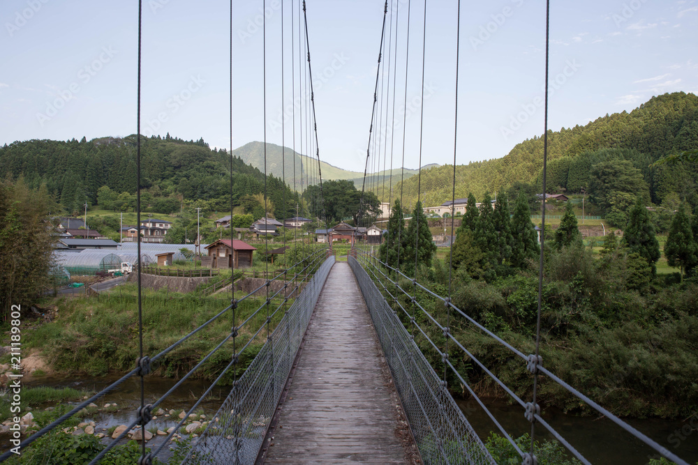 Obraz premium Narrow suspension bridge leading to small Japanese village with Soni Kogen visible in the background