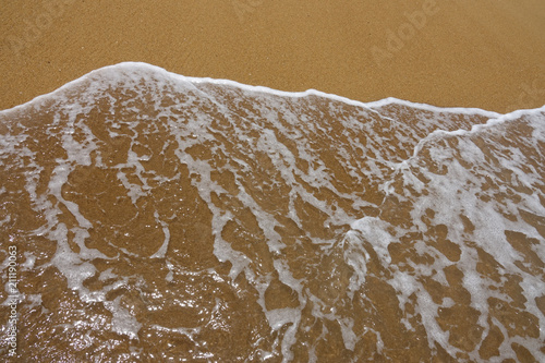 Wave of the sea with white foam against the background of a sandy beach. View from above