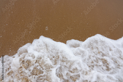 Wave of the sea with white foam against the background of a sandy beach. View from above