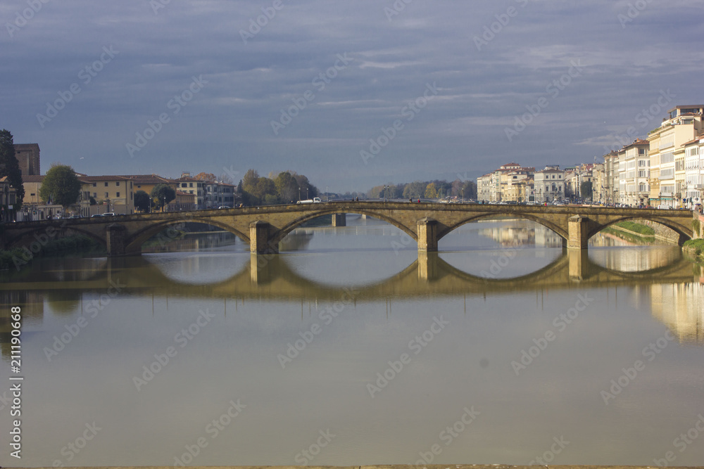 Frontal view of Carraia bridge in Florence on Arno river, with its reflection on water