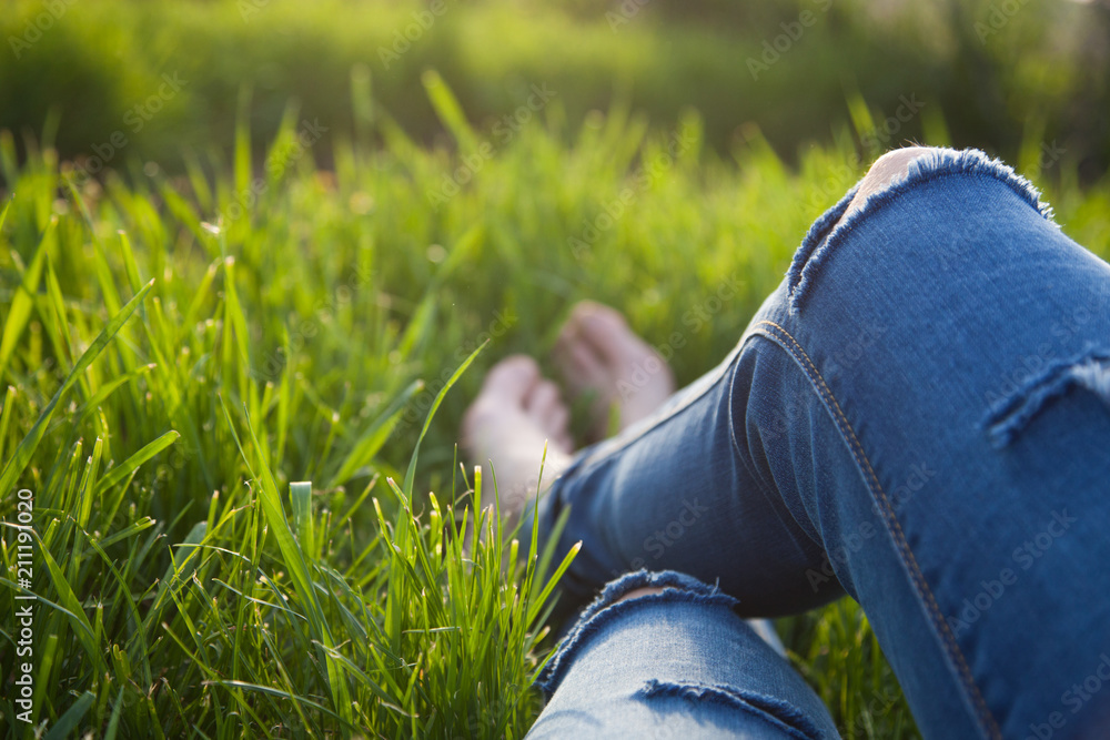 legs of hipster woman wearing torn jeans lying in green grass with smartphone and headsets enjoying sunset - summertime relaxation legs of hipster woman wearing torn jeans lying in green grass with smartphone and headsets enjoying sunset - summertime relaxation